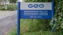 A blue sign that says “Geo Moshannon Valley Processing Center” in front of green leaves.