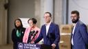 News conference featuring Governor Josh Shapiro at a podium, flanked by three individuals in a spacious industrial setting with cardboard boxes in the background.