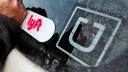 In this 2018, file photo, a Lyft logo is installed on a car next to an Uber sticker in Pittsburgh.