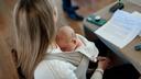 A woman sits while an infant rests on her chest.