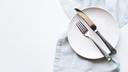 A stock image of an empty plate and cutlery on a white table.