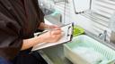 A stock image of a person with a clipboard in a kitchen.