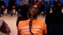 A student with long hair in a braid wears an orange T-shirt that says "taking a stand against gun violence."