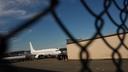 An airplane and a building seen through a chain link fence.