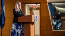 Jennifer Higgins, then-USCIS deputy director, swears in new citizens while raising her hand at a podium with the USCIS seal.