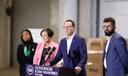 News conference featuring Governor Josh Shapiro at a podium, flanked by three individuals in a spacious industrial setting with cardboard boxes in the background.