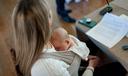 A woman sits while an infant rests on her chest.