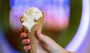 A hand holds a waffle cone with ice cream scoops