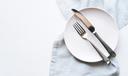 A stock image of an empty plate and cutlery on a white table.
