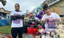 A man and woman stand at a memorial of flowers, balloons, and candles.