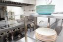 A stock image of plates stacked on a stainless steel shelf in a kitchen. A stock image of plates stacked on a stainless steel shelf in a kitchen.