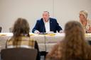 Aging Secretary Jason Kavulich speaks into a microphone during a meeting, with attendees in the foreground and a woman seated beside him.