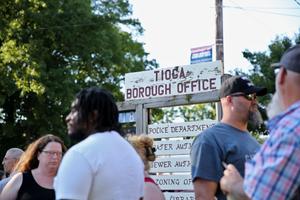 People stand in front of the Tioga Borough Office sign on a July day.