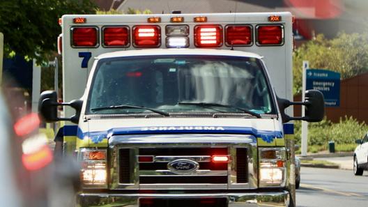 An ambulance seen head on with its lights on in the daylight.
