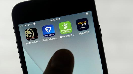 FanDuel, DraftKings, and other online gambling apps are displayed on a phone.