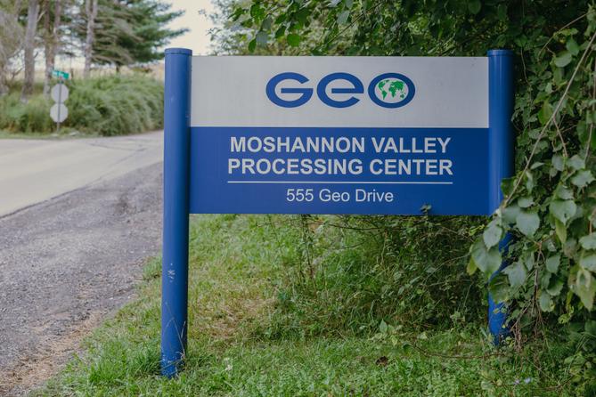 A blue sign that says “Geo Moshannon Valley Processing Center” in front of green leaves.
