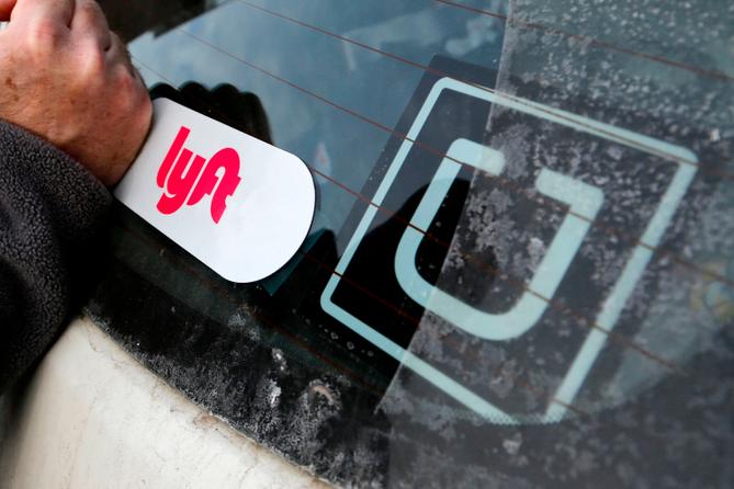 In this 2018, file photo, a Lyft logo is installed on a car next to an Uber sticker in Pittsburgh.