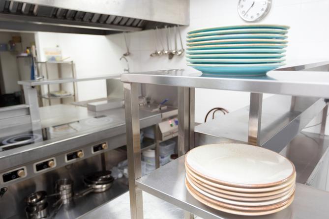 A stock image of plates stacked on a stainless steel shelf in a kitchen.