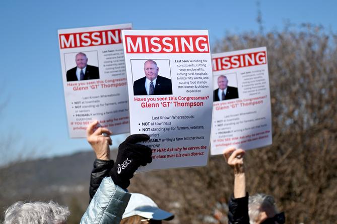 People hold up signs of U.S. Rep. Glenn Thompson that say “missing” during a protest outside his Bellefonte office.
