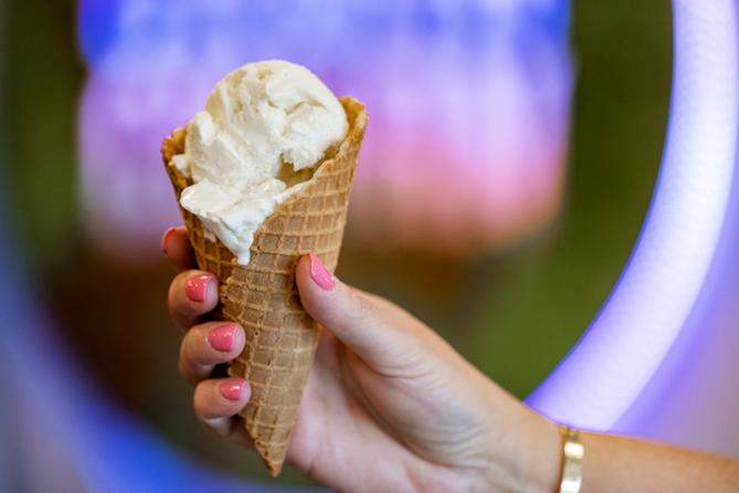 A hand holds a waffle cone with ice cream scoops
