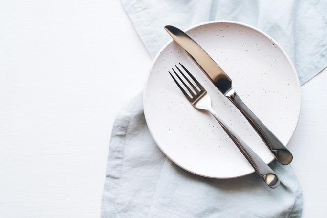 A stock image of an empty plate and cutlery on a white table. A stock image of an empty plate and cutlery on a white table.