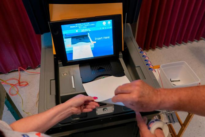 A polling judge, right, helps guide a voter's ballot into a voting machine during the Pennsylvania primary election, at Mont Alto United Methodist Church in Alto, Pa., on May 17, 2022.