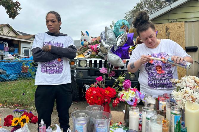 A man and woman stand at a memorial of flowers, balloons, and candles. A man and woman stand at a memorial of flowers, balloons, and candles.