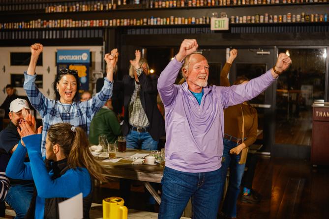 A woman and a man raise their arms in celebration as people around them clap. A woman and a man raise their arms in celebration as people around them clap.