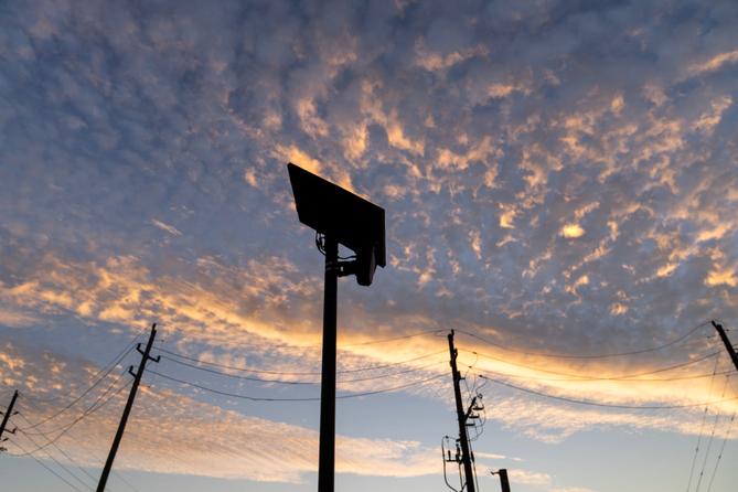 Silhouetted Flock Safety license plate reader against an orange-and-blue sunset sky, with utility poles and power lines below. Silhouetted Flock Safety license plate reader against an orange-and-blue sunset sky, with utility poles and power lines below.