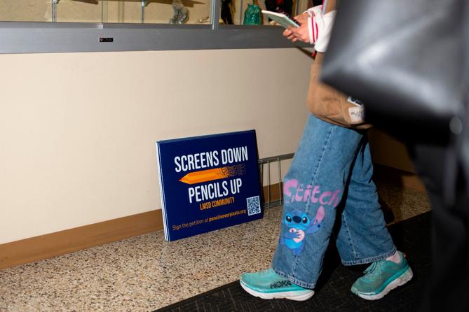 Signs reading, "Screens down, pencils up," are seen a school board meeting at the Lower Merion School District Administration Building on Monday, May 11, 2026, in Ardmore, Pa.
